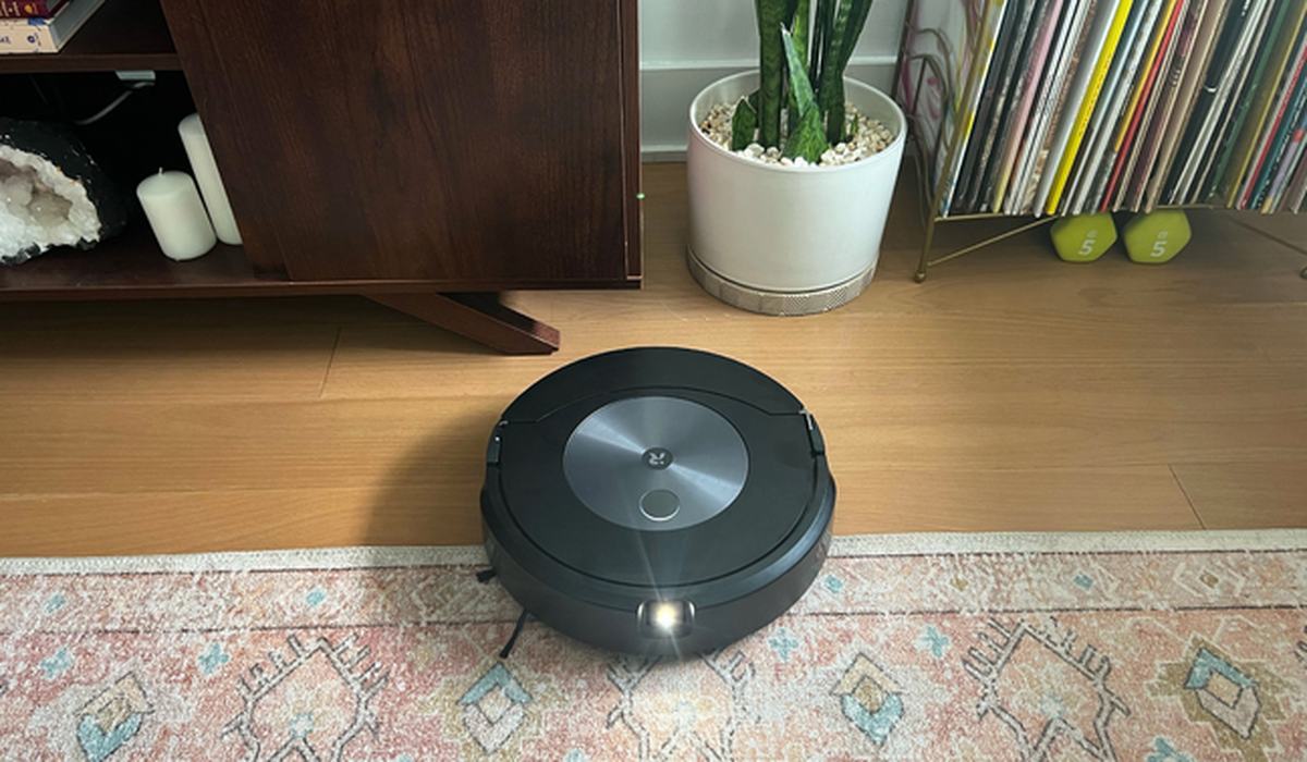 Robot vacuum cleaning a wood floor beside a rug in an apartment