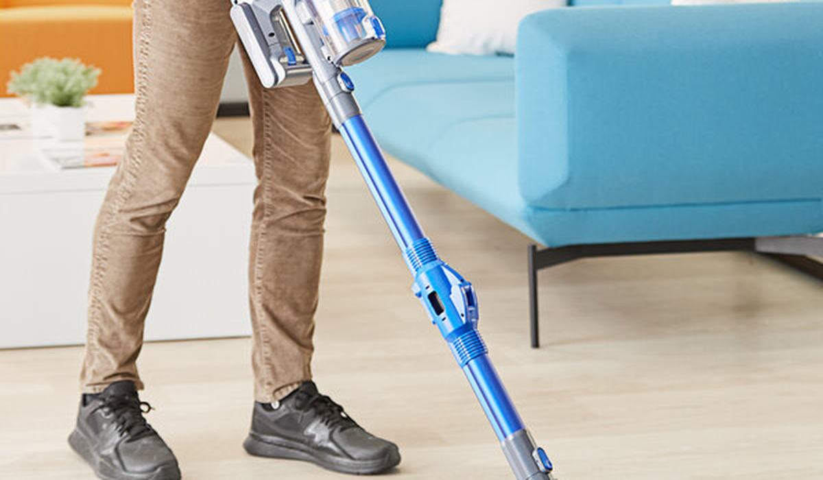 Person using a cordless stick vacuum on a wood floor in an apartment